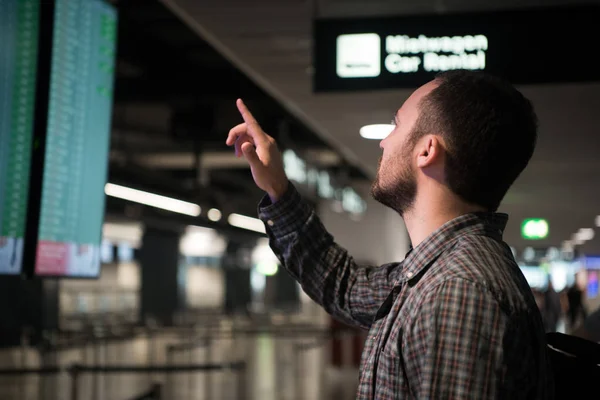 Homem apontando com um dedo no horário de voo desfocado para verificar o horário de partida no terminal do aeroporto internacional com espaço de cópia . — Fotografia de Stock