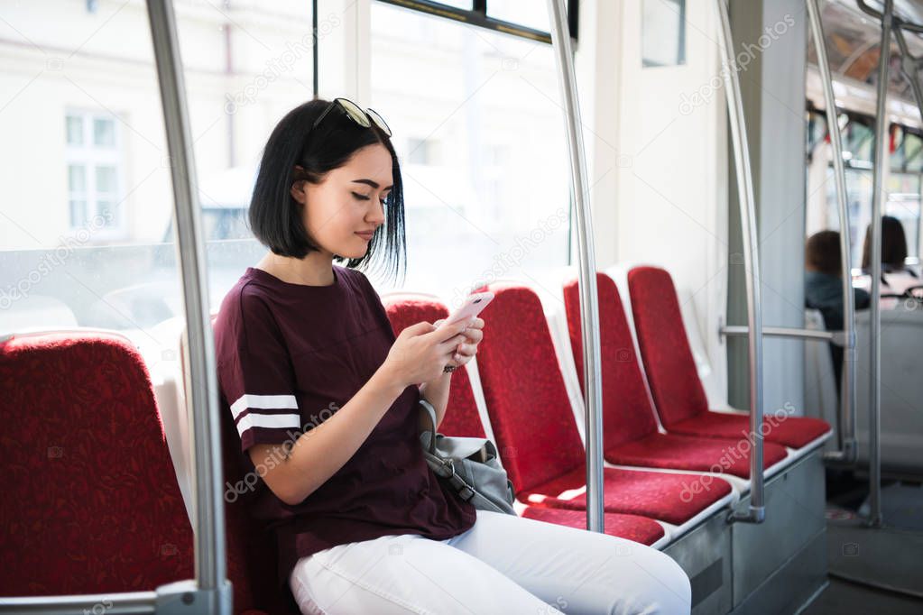 Young beautiful woman browsing and typing messages in a public bus.