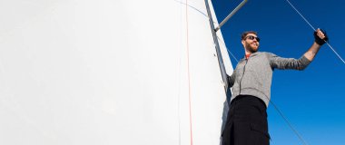 Yat Kaptan sakallı bir yelkenli yatta yelken boom duruyor ipi elinde tutan ve gülümseyerek, mutlu hissediyor. Yetişkin yachtsman dünya çapında seyahat. Kopya alanı