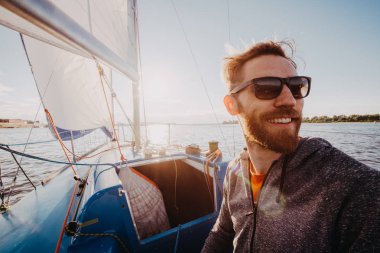 Adam rahat kıyafet ve güneş gözlüğü bir yatta giymiş. Mutlu yetişkin sakallı yachtsman yakın çekim portre. Bir deniz veya nehir regata sırasında gülümseyen bir teknede yakışıklı denizci.