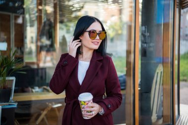 Esmer kız çarpıcı yaşam tarzı moda portre açık havada. Gülümseyen, kahve içme ve şehrin sokak yürüyüş. Alışveriş gidiyor. Trendsetter. Şık Bordo büyük boy palto giyiyor