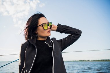 Güzel esmer kız bir gökyüzü arka plan ve okyanus üzerinde siyah ceket. Yat ve tekne seyahat
