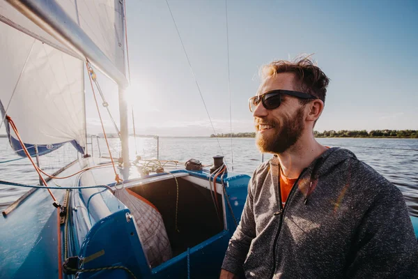 Успешный молодой бородатый мужчина, парусный портрет на восходе солнца на лодке — стоковое фото