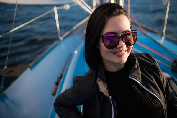 Jovem sorrindo mulher de cabelos escuros usando óculos escuros sentados em um barco no dia ensolarado de outono, andando em um mar ou rio — Fotografia de Stock