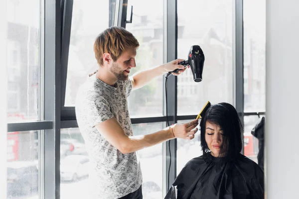 Smiling woman getting haircut by handsome hairdresser