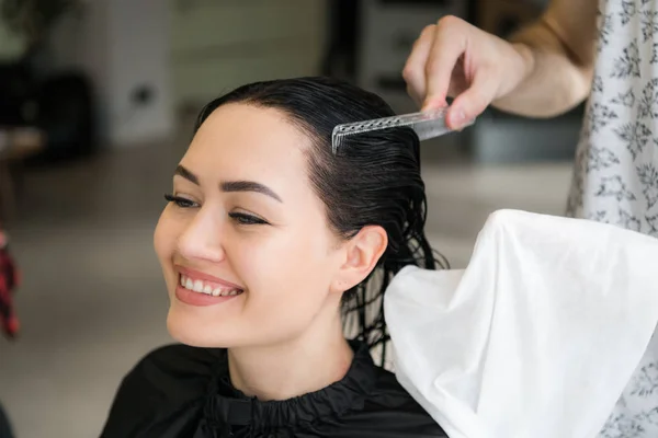 Fiatal, boldog, szép nő mosolyog a kamerába, miközben profi fodrász csomagolás a nedves haját egy törülközőt a sampon lemosást követően közelről — Stock Fotó