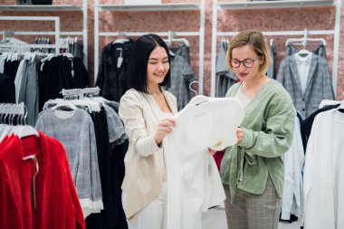 Satış Danışmanı yardım giyim mağaza müşteri için seçer. Stilist kavramı ile alışveriş. Kadın tezgâhtar ve genç kadın moda butik