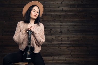 Eğleniyor ve ahşap studio arka plan üzerinde küçük ukulele gitar ile poz genç hippi kız.