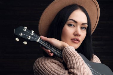 Ukulele ahşap arka plan önünde oynayan genç kafkas kadın portresi kapatın. Stüdyo çekim, boş zaman faaliyetleri kavramı.