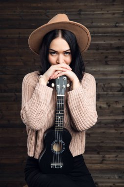 ahşap duvar arka plan üzerinde kapalı bir ukulele ile şapkalı bir kadın