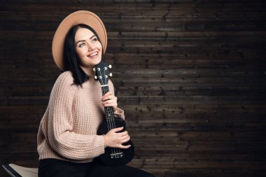 ahşap duvar arka plan üzerinde kapalı bir ukulele ile şapkalı bir kadın