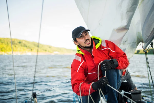 Stilig man på yacht vidrör vita segel kallas assymetrisk spinnaker, arbetar med talja i havet vid sommardag, under vy. — Stockfoto