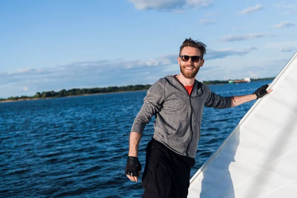 Handsome man traveling by yacht. Casual outfit, man dressed in grey hoodie, spring time, bearded man in sunglasses on the boat.