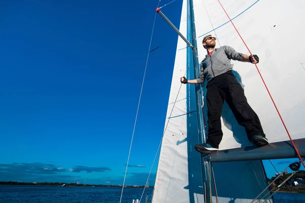 Young seaman on a sailboat standing on a sail boom. Captain of the yacht in the open sea.