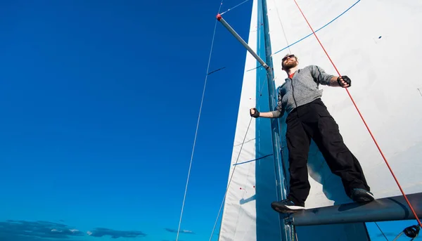 Young seaman on a sailboat standing on a sail boom. Captain of the yacht in the open sea.