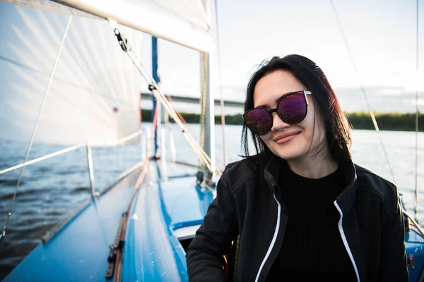 Młoda kobieta Ciemnowłosa uśmiechający się, noszenie okularów przeciwsłonecznych, siedzi na pokładzie łodzi w słoneczny dzień jesienny, chodzenie na morzu lub rzece — Zdjęcie stockowe