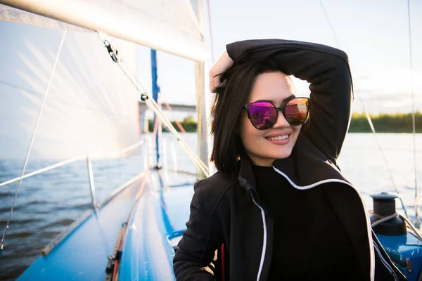Młoda kobieta Ciemnowłosa uśmiechający się, noszenie okularów przeciwsłonecznych, siedzi na pokładzie łodzi w słoneczny dzień jesienny, chodzenie na morzu lub rzece — Zdjęcie stockowe