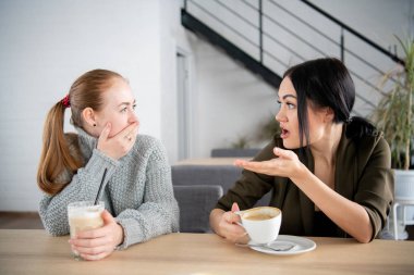 Mutsuz bayan arkadaş şok edici haberleri tartışmak. Ağız kapsayan ve café'de birbirine bakarak iki şok genç kadın. Duygusal bir tepki kavramı