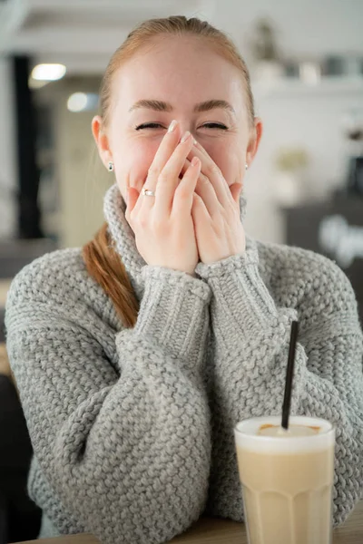 笑みを浮かべてテーブルのカフェで座っている若い笑顔の女性は、彼女の口に手します。流行に敏感な生姜、あくび、手で彼の口を覆っています。. — ストック写真