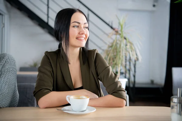 Joven mujer de negocios bonita bebiendo café en la oficina, al lado de la ventana de cristal — Foto de Stock