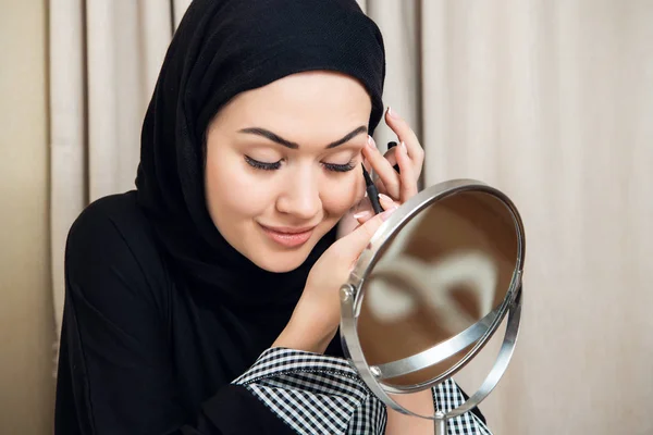 Hermosa mujer musulmana aplicando delineador de ojos en casa — Foto de Stock