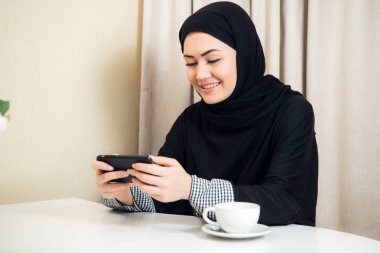 Evde bir akıllı telefon kullanan Arap mutlu rahat kadın