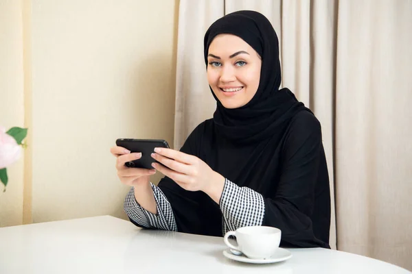 Mujer árabe bastante moderna jugando en el teléfono inteligente en casa — Foto de Stock