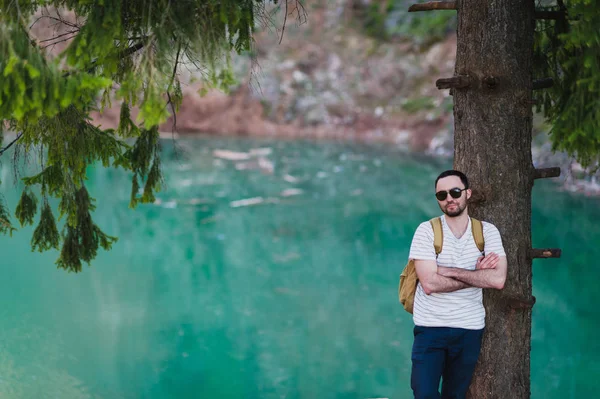Hombre guapo sobre la naturaleza verde y el lago azul de pie cerca del árbol. Aventura, viajes, turismo y ocio - niño relajándose en el bosque . —  Fotos de Stock