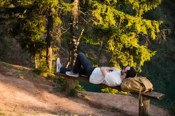 Mann ruht beim Wandern auf einer Holzbank im Wald. Wandern in der Natur — Stockfoto