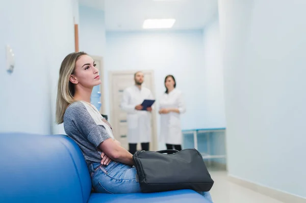 Mujer esperando en el pasillo de un hospital los resultados de una prueba. Me siento nervioso. Médicos hablando en un segundo plano . — Foto de Stock