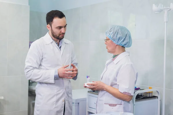 Químicos jóvenes y mayores trabajando juntos y mirando un tubo de ensayo en un laboratorio clínico — Foto de Stock