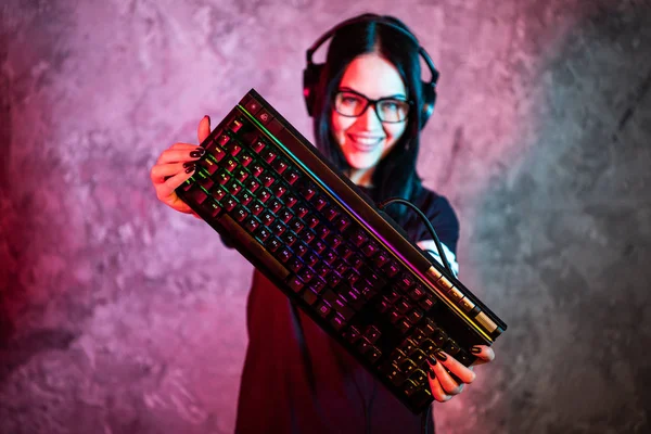Όμορφη φιλική Pro Gamer Streamer κορίτσι Posing με ένα πληκτρολόγιο στα χέρια της, φορώντας γυαλιά. Ελκυστικό Geek κορίτσι με δροσερό νέον ρετρό χρώματα στο παρασκήνιο. — Φωτογραφία Αρχείου