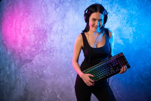 Beautiful Friendly Pro Gamer Streamer Girl Posing With a Keyboard in Her Hands, Wearing Glasses. Attractive Geek Girl with Cool Neon Retro Colors in Background. — Stock Photo, Image