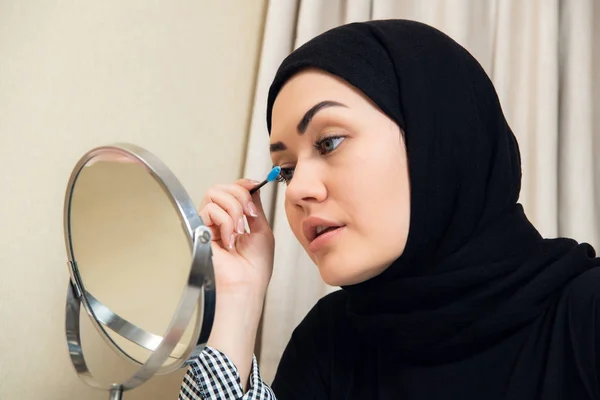 Kauneus musliminainen hijab soveltamalla meikkiä. Kaunis tyttö katselee peiliin ja soveltamalla kosmeettisia. Tyttö punastuu poskipäille . — kuvapankkivalokuva