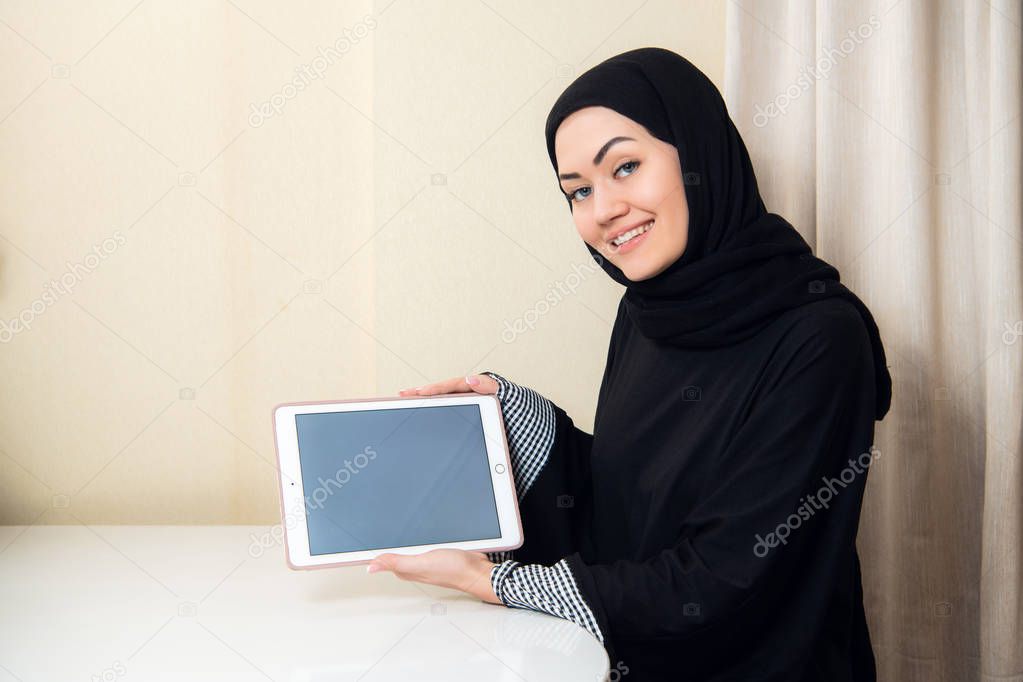 Muslim woman holding tablet with blank screen at home or office. Technology copyspace concept