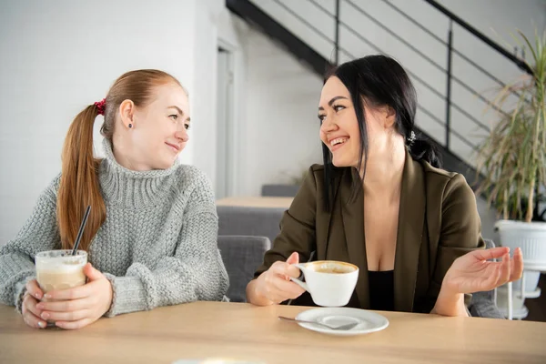 Dos mujeres jóvenes y hermosas se reúnen en el bar para un capuchino y charlar . — Foto de Stock