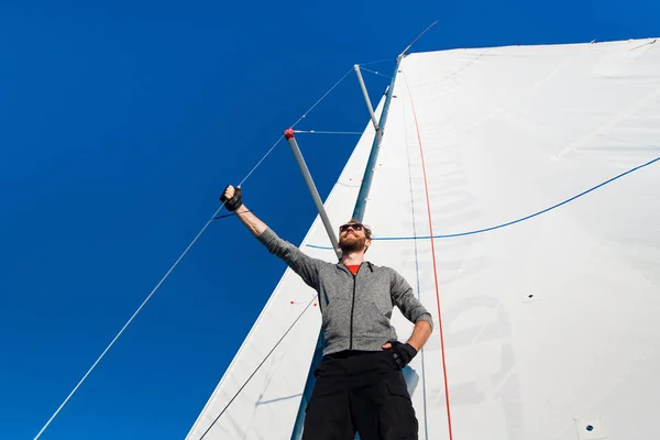 Yacht kapitány szakáll áll egy vitorlás hajó, vitorlás fellendülés a kötél tartja a kezében, és mosolyogva, boldogok. Felnőtt yachtsman utazik szerte a világban. Másolja a hely — Stock Fotó