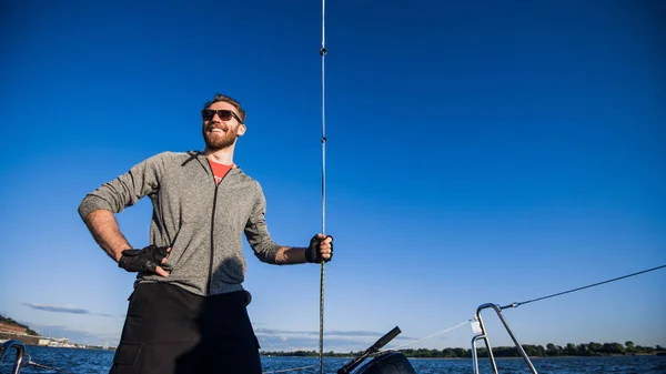 一个戴着太阳镜的英俊的胡须男人在河上或湖上的船上。美丽快乐的家伙在船上游泳在秋天阳光明媚的日子感觉自由享受生活 — 图库照片