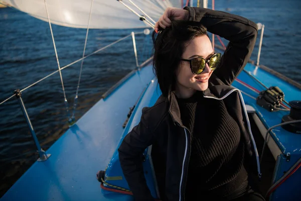 Genç gülümseyen esmer kadın güneşli bir sonbahar günde tekne bir gemide otururken, bir deniz veya nehir üzerinde yürürken güneş gözlüğü takıyor