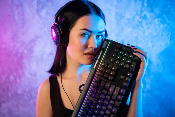 Νέοι σέξι ντίσκο κορίτσι φορώντας ακουστικά τυχερού παιχνιδιού κρατώντας πληκτρολόγιο τυχερού παιχνιδιού. Δωμάτιο αναμμένα στο ρετρό, Retrowave ή Cyberpunk στυλ με νέον και ροζ φώτα. — Φωτογραφία Αρχείου