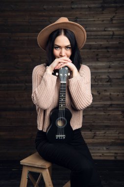 Genç kız bir ukulele ile gülümseyen Studio ahşap arka plan üzerinde oturmak.