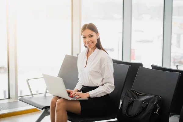 Mujer casual trabajando en el portátil en la sala del aeropuerto. Mujer esperando su vuelo en la terminal del aeropuerto, sentado en la silla y escribiendo en el portátil . — Foto de Stock