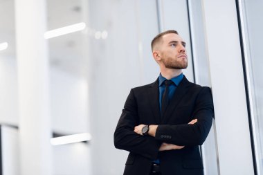 Pencerenin yanında elleri çapraz olan kendine güvenen bir iş adamının portresi..