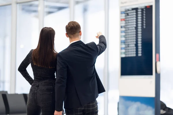 Young couple in international airport looking at the flight information board, checking her flight — 스톡 사진