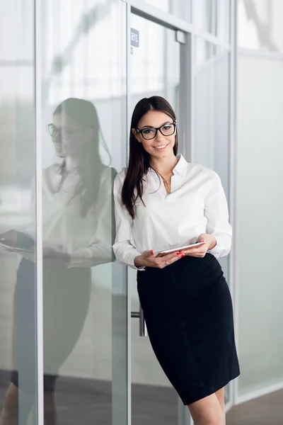 Mujer de negocios con blusa blanca de pie en el pasillo de la oficina con la tableta y sonriendo. — Foto de Stock