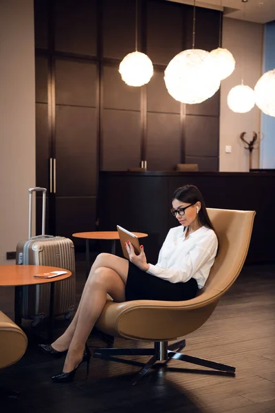 Mujer de negocios segura escuchando música en su tableta mientras está sentada en la silla en la sala de negocios del aeropuerto —  Fotos de Stock