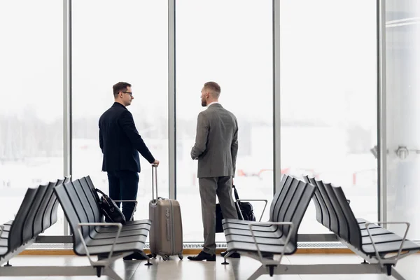 Силуэт двух бизнесменов, стоящих перед большим окном в аэропорту у ворот вылета — стоковое фото