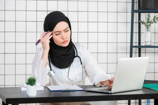중년 선배 아랍 간호사 여성은 의학 사무실에서 히잡을 쓰고 턱에 손을 얹고 질문, 펜시브 표현을 생각하고 있습니다. 의심 개념. — 스톡 사진