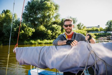 Sakallı yakışıklı bir teknede bir nehir ya da göl güneş gözlüğü. Bir botla ücretsiz hayattan zevk bir sonbahar güneşli gün hisse yüzme güzel mutlu adam