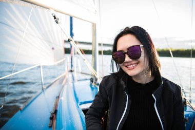 Güzel esmer kız bir gökyüzü arka plan ve okyanus üzerinde siyah ceket. Yat ve tekne seyahat